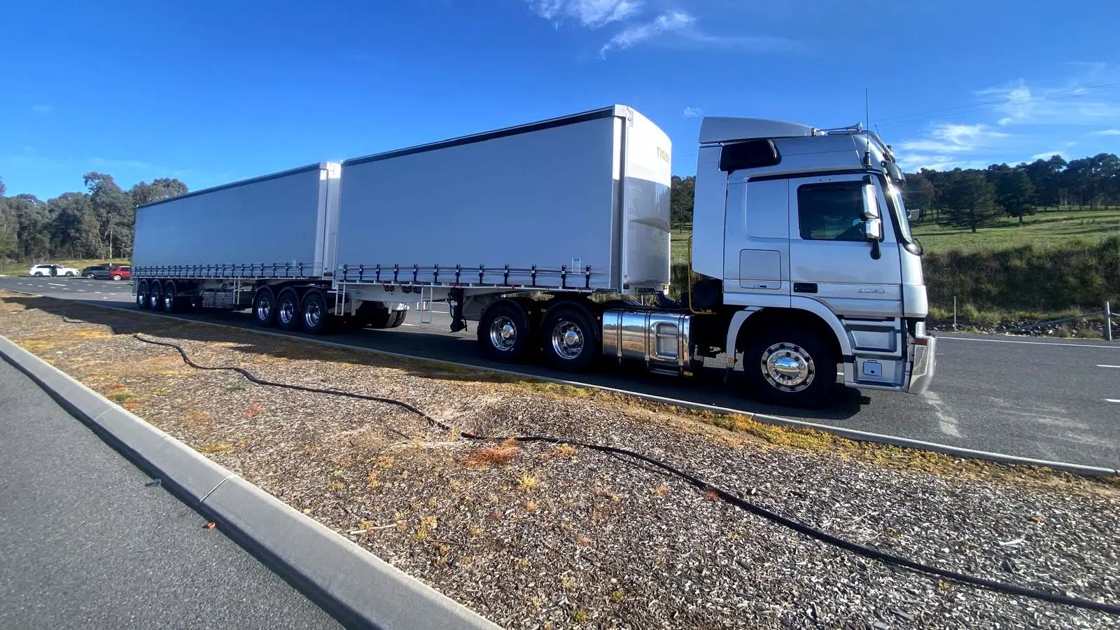 A Digiton prime mover and B-Double pulled up on a highway shoulder, gum trees and open paddock behind it.
